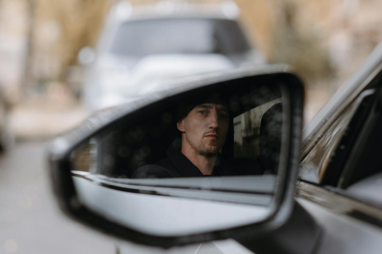 Man looking at side mirror of the car.