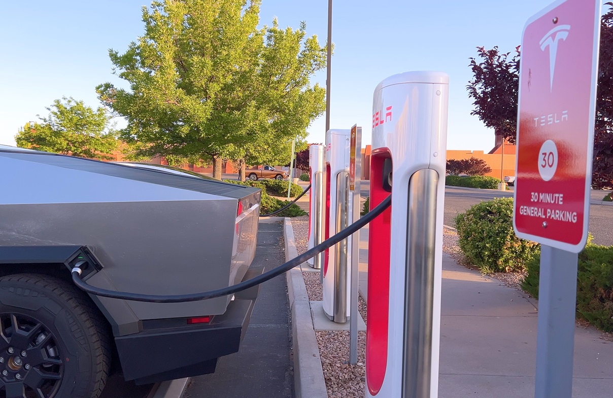 A Tesla Cybertruck is connected to a Tesla Supercharger at an outdoor charging station - 2024