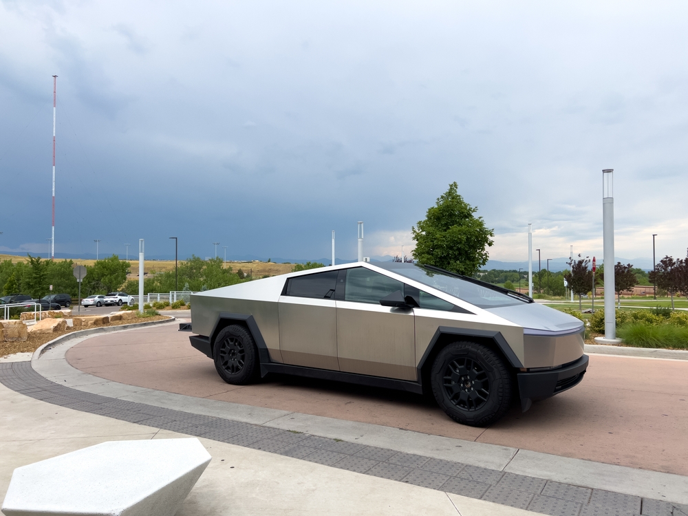 A sleek Tesla Cybertruck is parked outdoors against a backdrop of a cloudy sky.