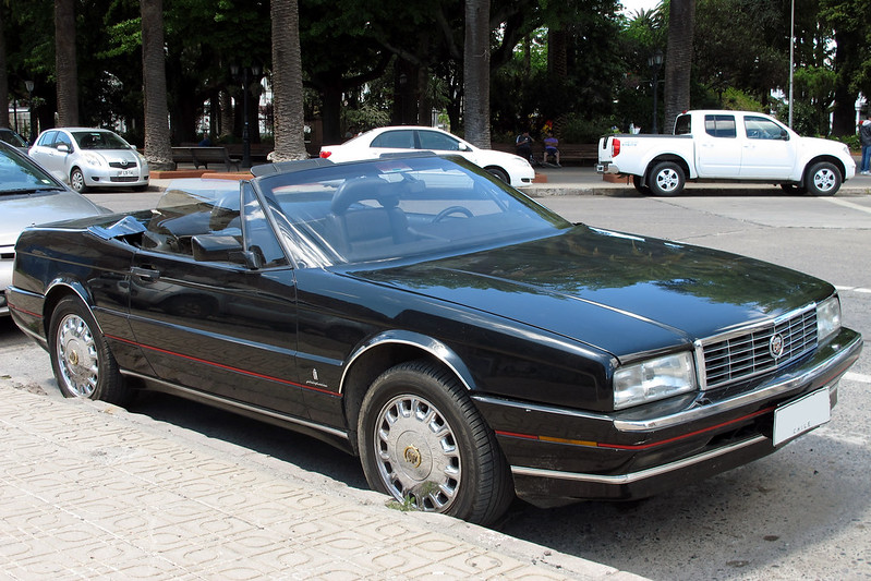 A close-up photo of a Black 1991 Cadillac Allante car parked on a city street