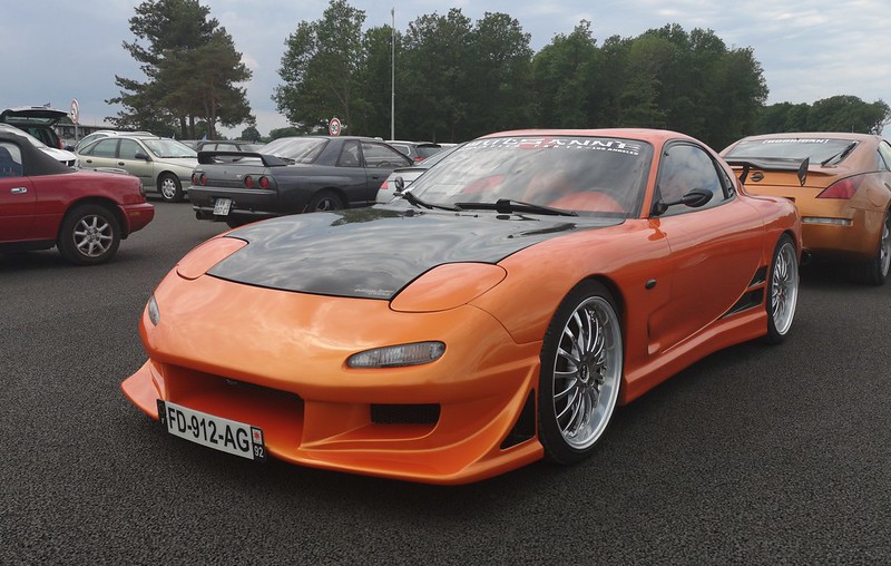 A close-up photo of a Orange 1992 Mazda RX7 car parked in a parking lot