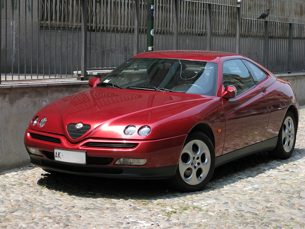 A close-up photo of a Red 1995 Alfa Romeo GTV car parked on a city street
