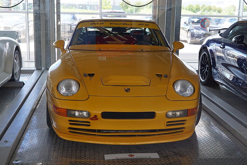 A close-up photo of a Yellow Porsche 968 Turbo car on display at an exhibition