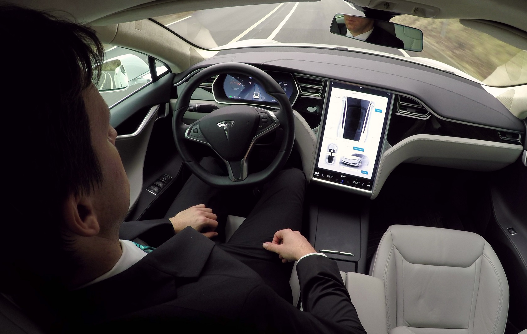 Young businessman traveling to work in luxury Tesla Model S car with enabled autopilot automated self-driving system - 2016