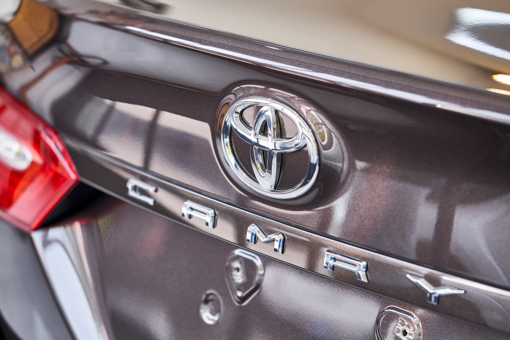 Toyota Camry trunk with shiny rear panel and reflection of logo on bonnet.
