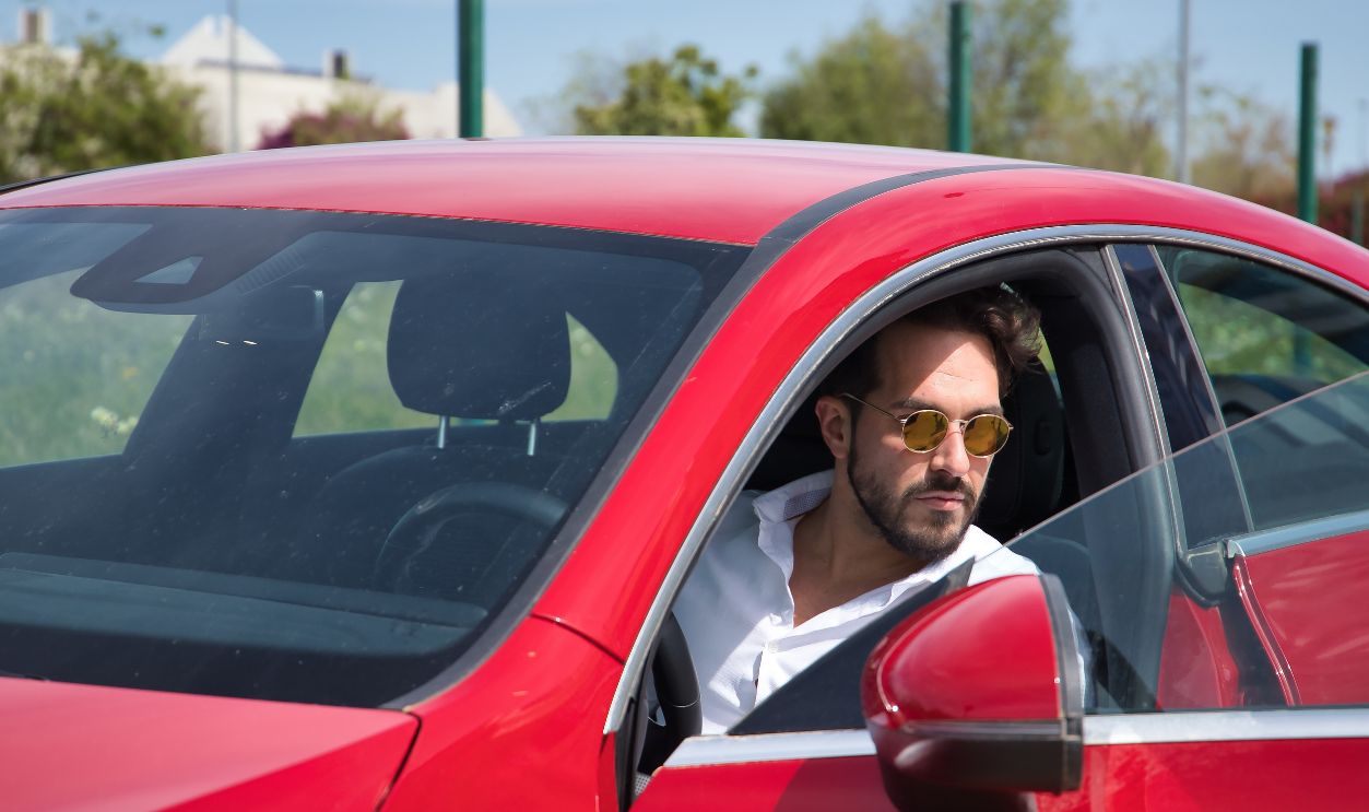 Handsome young man with beard, sunglasses and white shirt, inside his red sports car. Concept beauty, fashion, trend, luxury, motor, sports, winner.