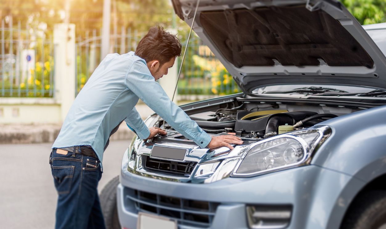 Man examining a broken car on a sunny day