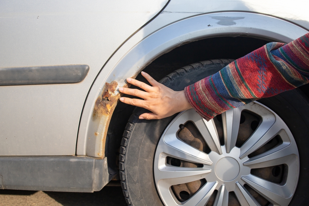A woman shows rust on a car door from winter reagents.