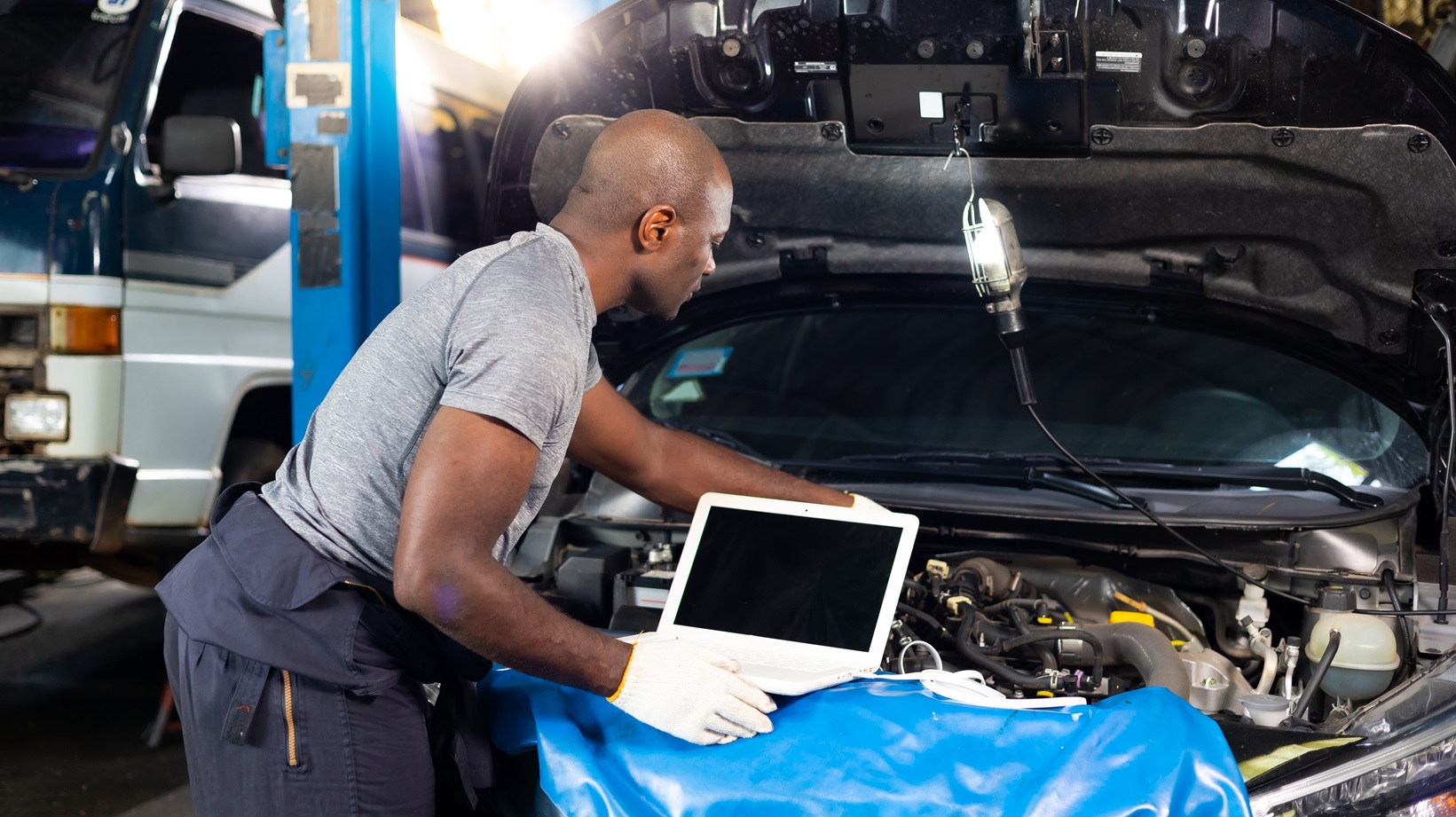 Professional car mechanic repair service and checking car engine by Diagnostics Software computer.
