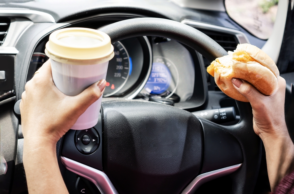 Woman's hand, holding burger and coffee while driving.