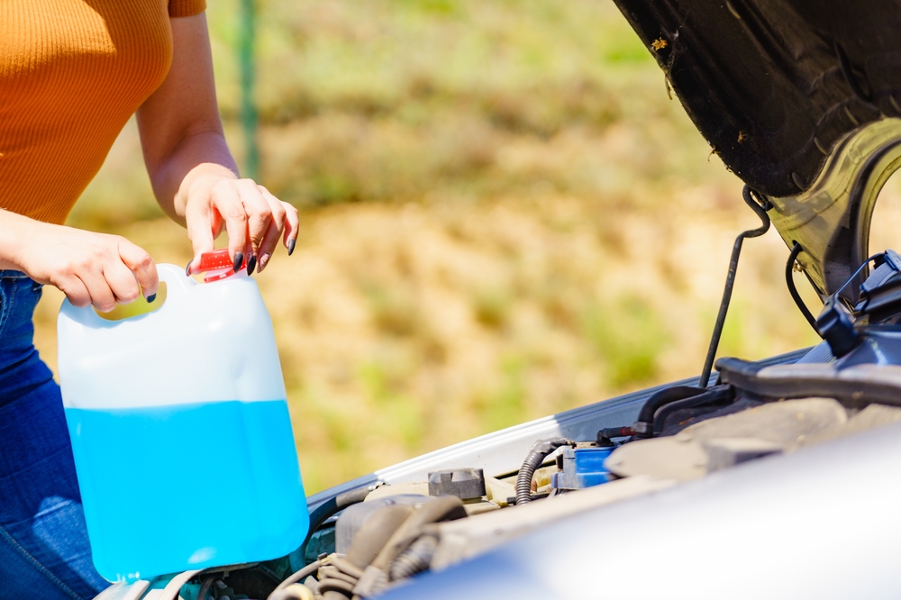Woman pouring blue antifreeze liquid for car windshield screen washing with bootle watering can