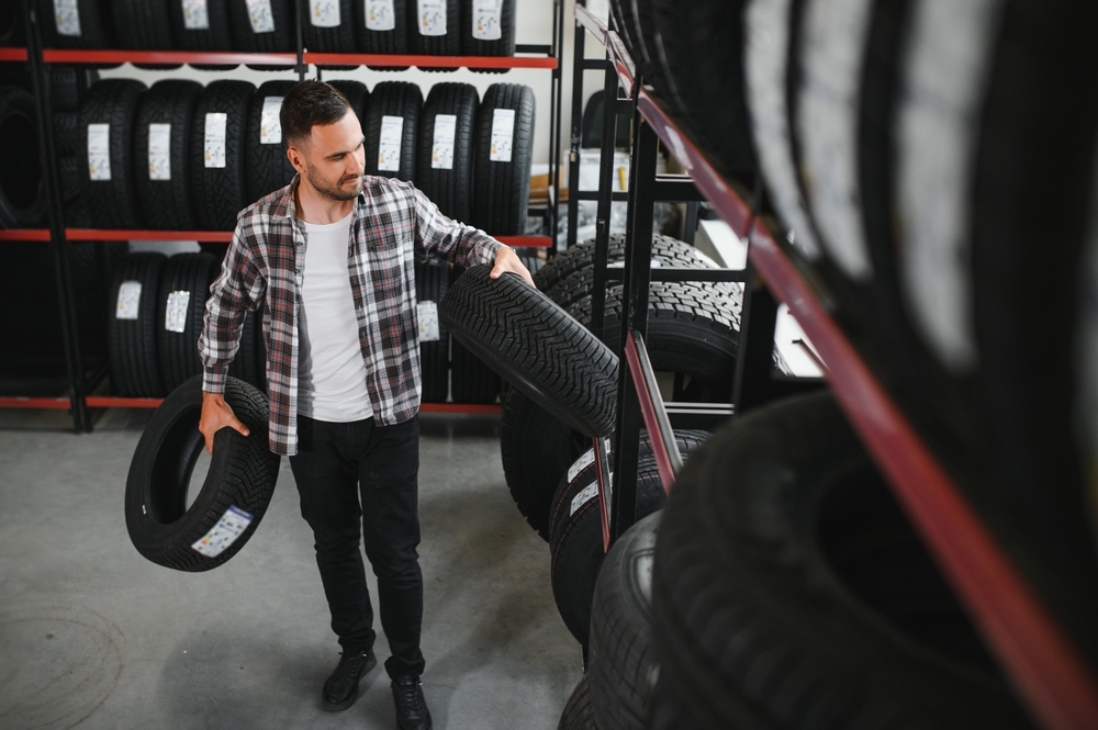 Customer examining brand and product characteristics while buying new tires in auto department of dealership.