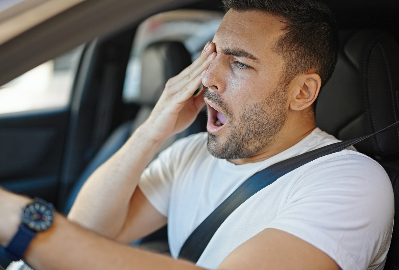 Tired man driving car and yawning at street.