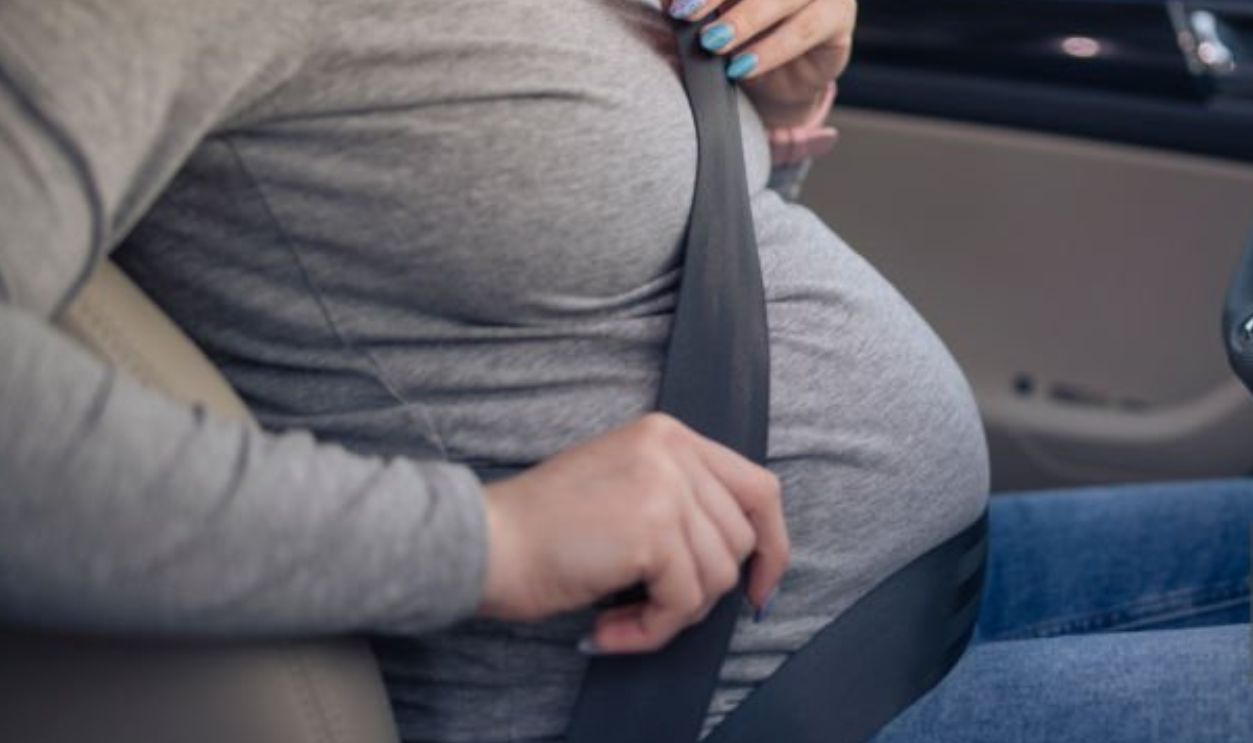 Unrecognisable pregnant woman adjusting seatbelt in a car.