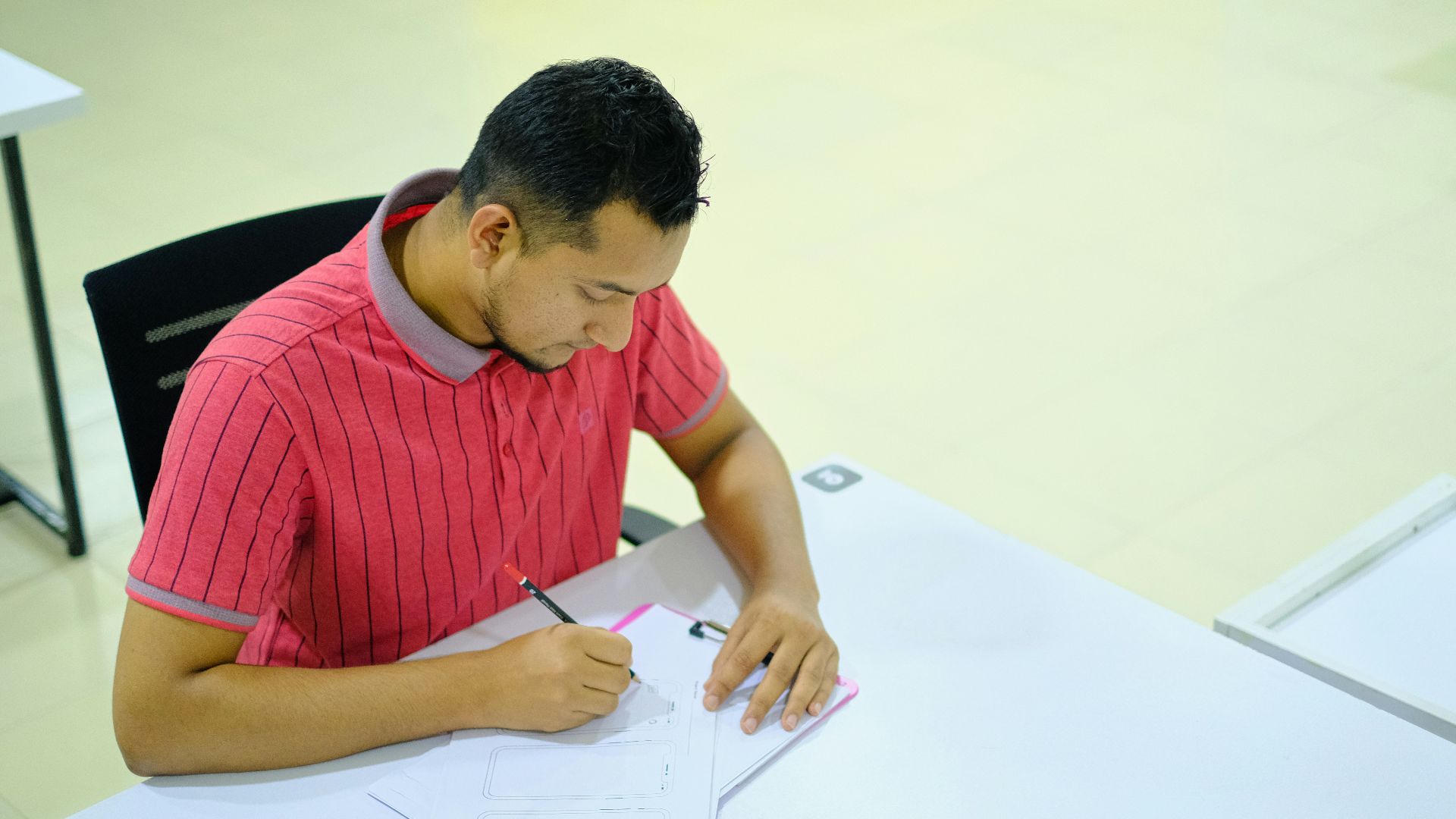 man in red and white striped crew neck t-shirt writing on white paper