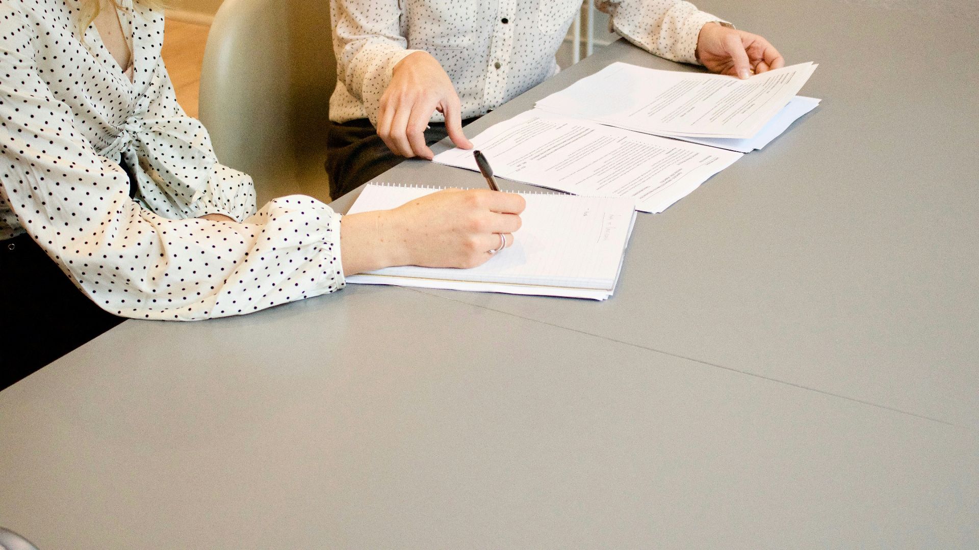 woman signing on white printer paper beside woman about to touch the documents