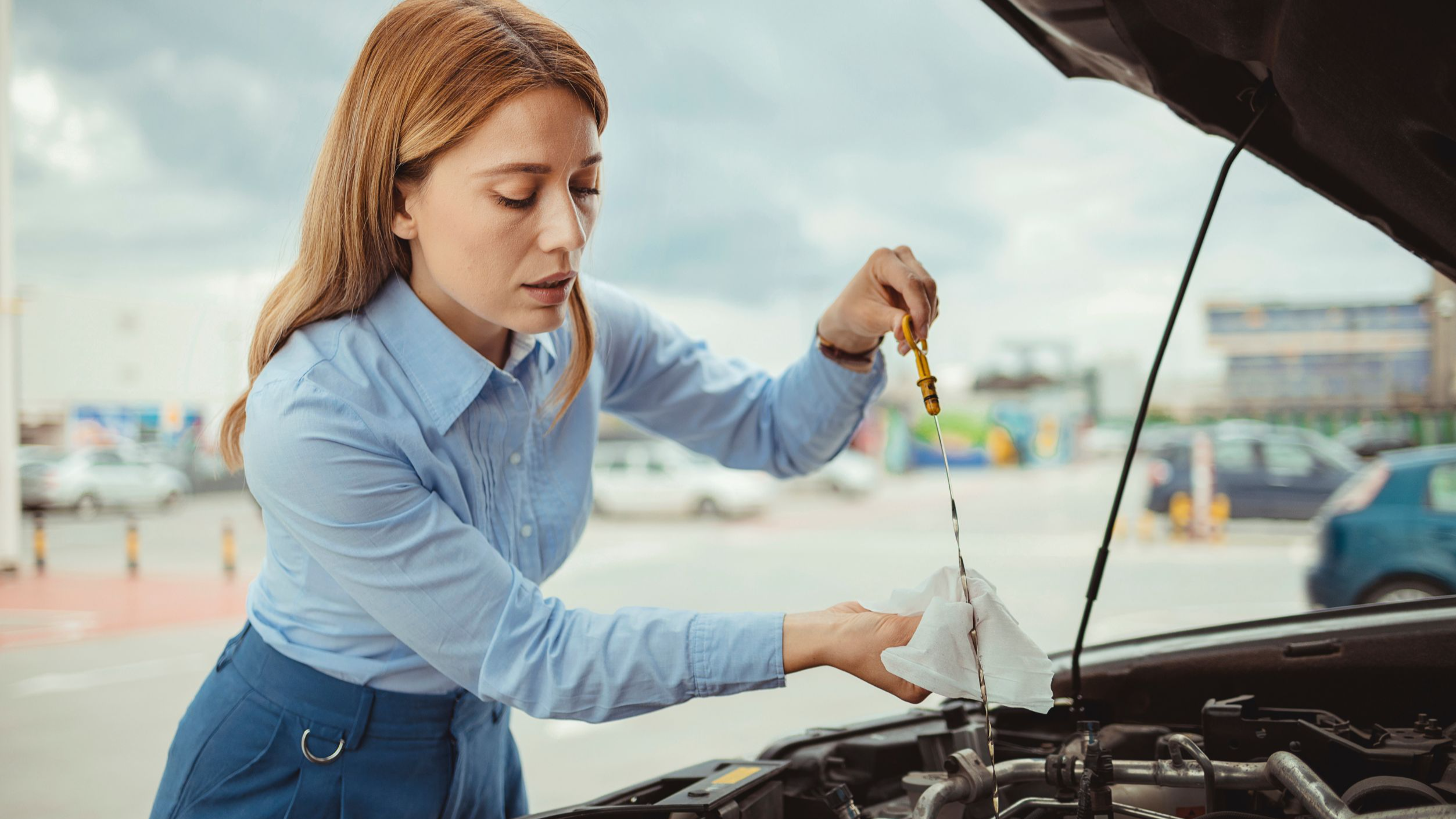 Woman driver checking level of oil on a car engine dipstick