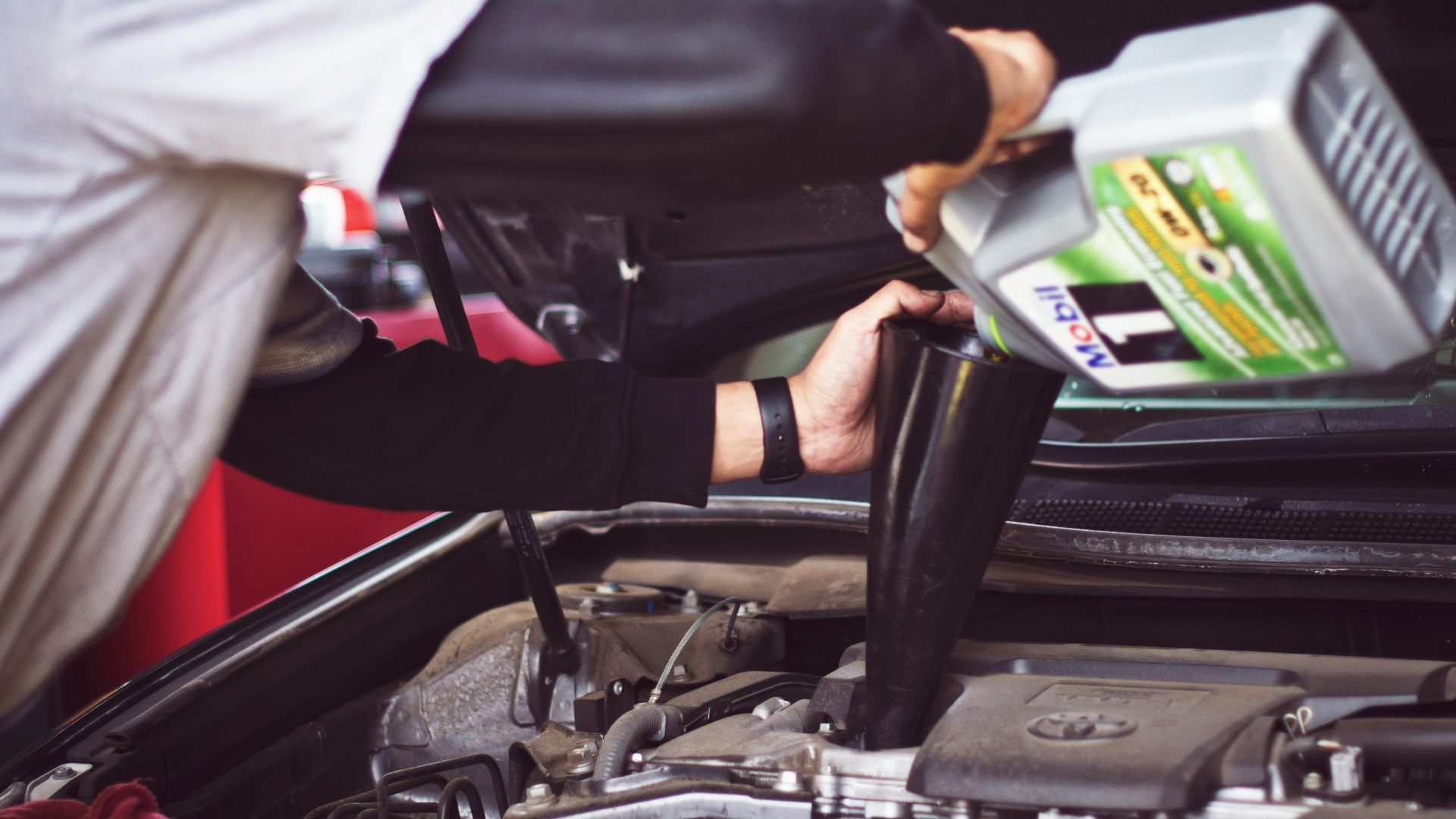 man refilling motor oil on car engine bay
