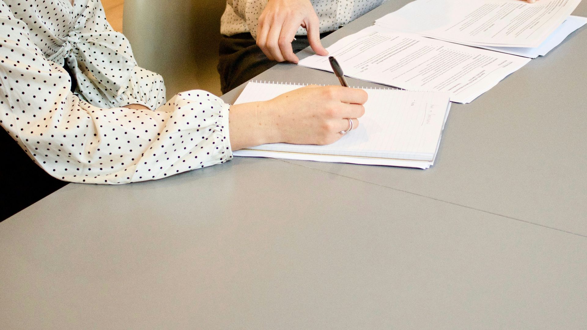 woman signing on white printer paper beside woman about to touch the documents
