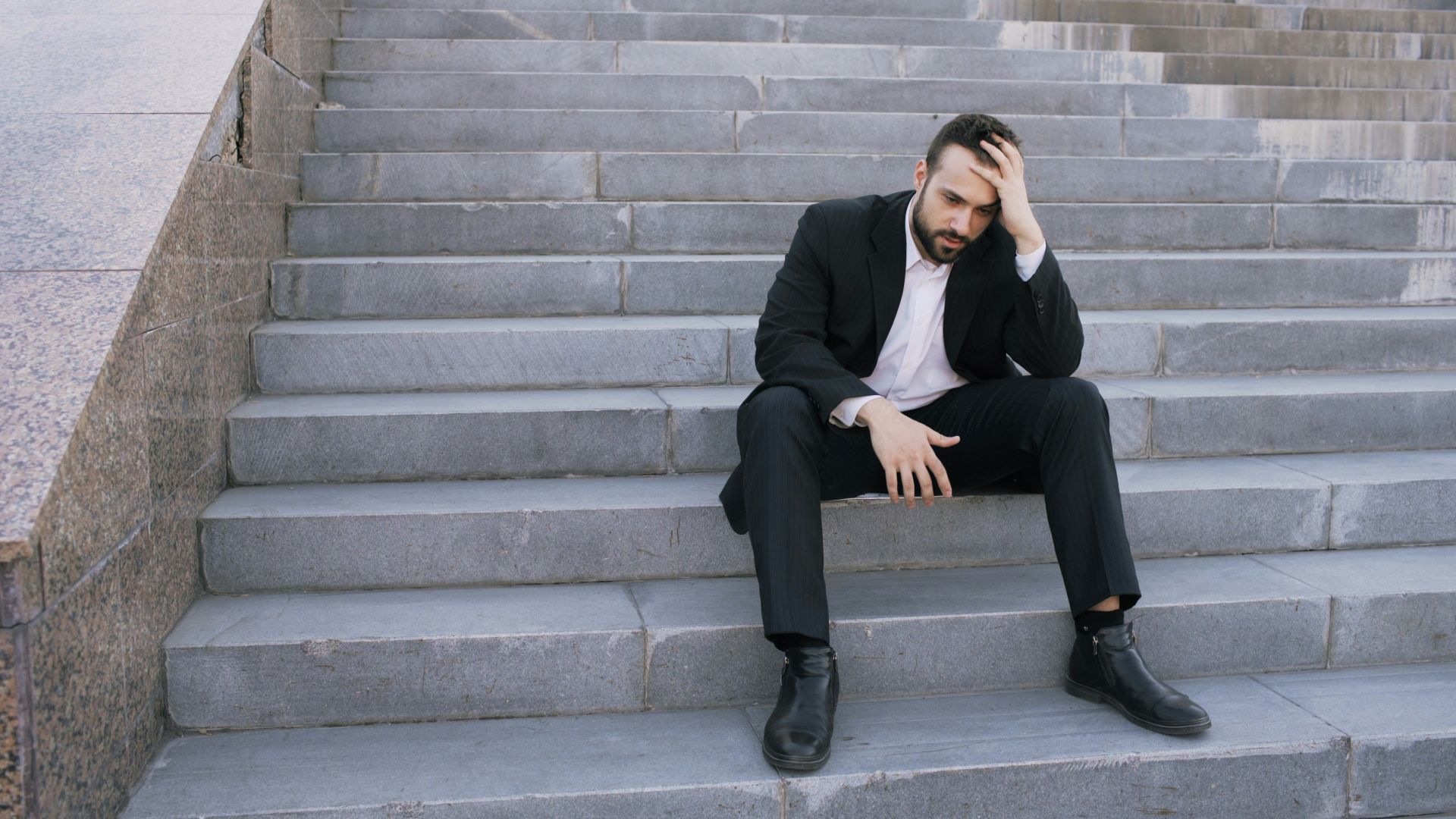 Man in suit sitting on steps, head in hand.