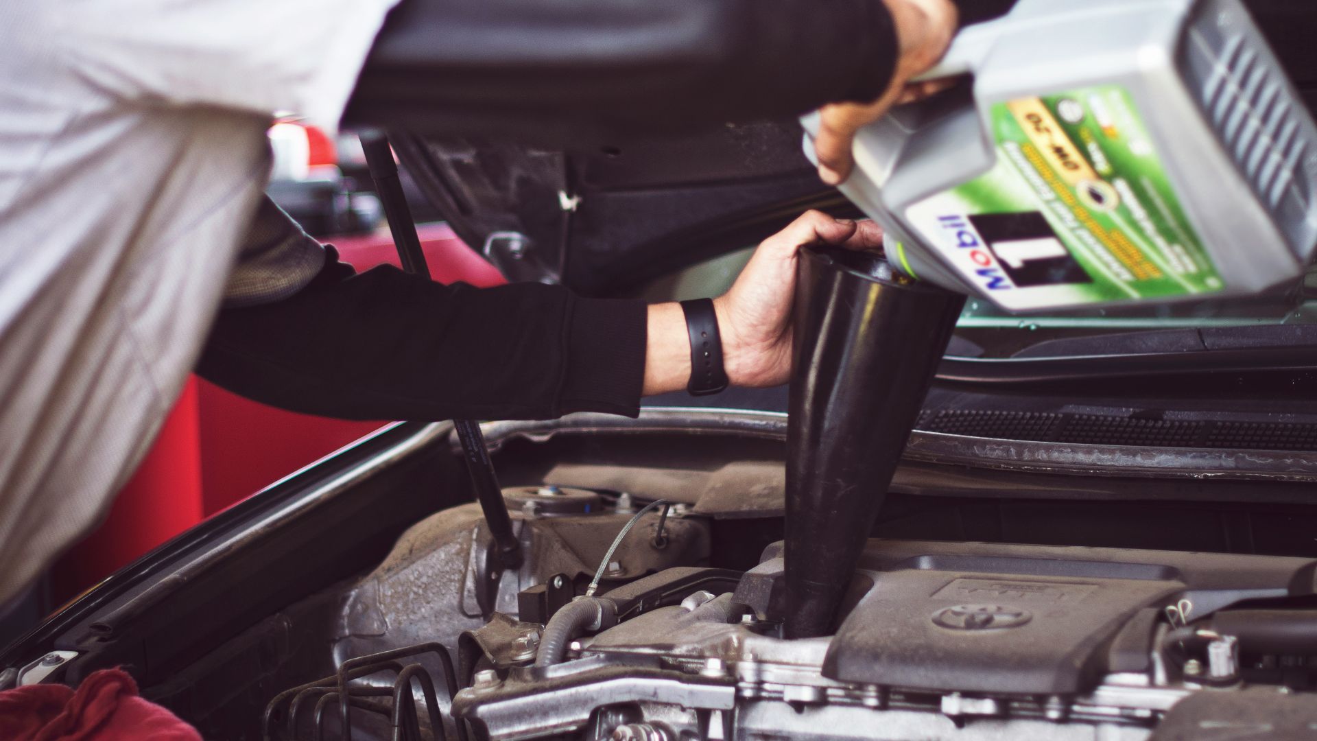 man refilling motor oil on car engine bay