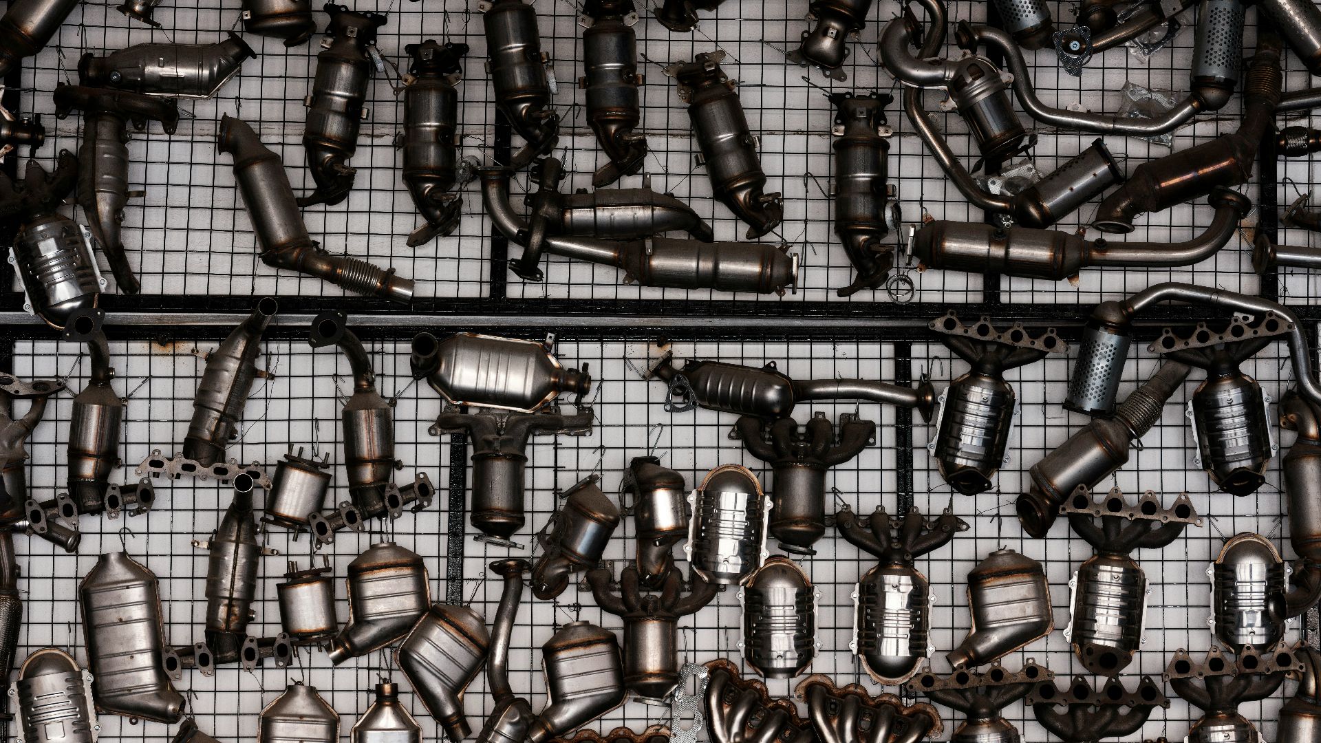 Many catalytic converters hanging on a grid wall.
