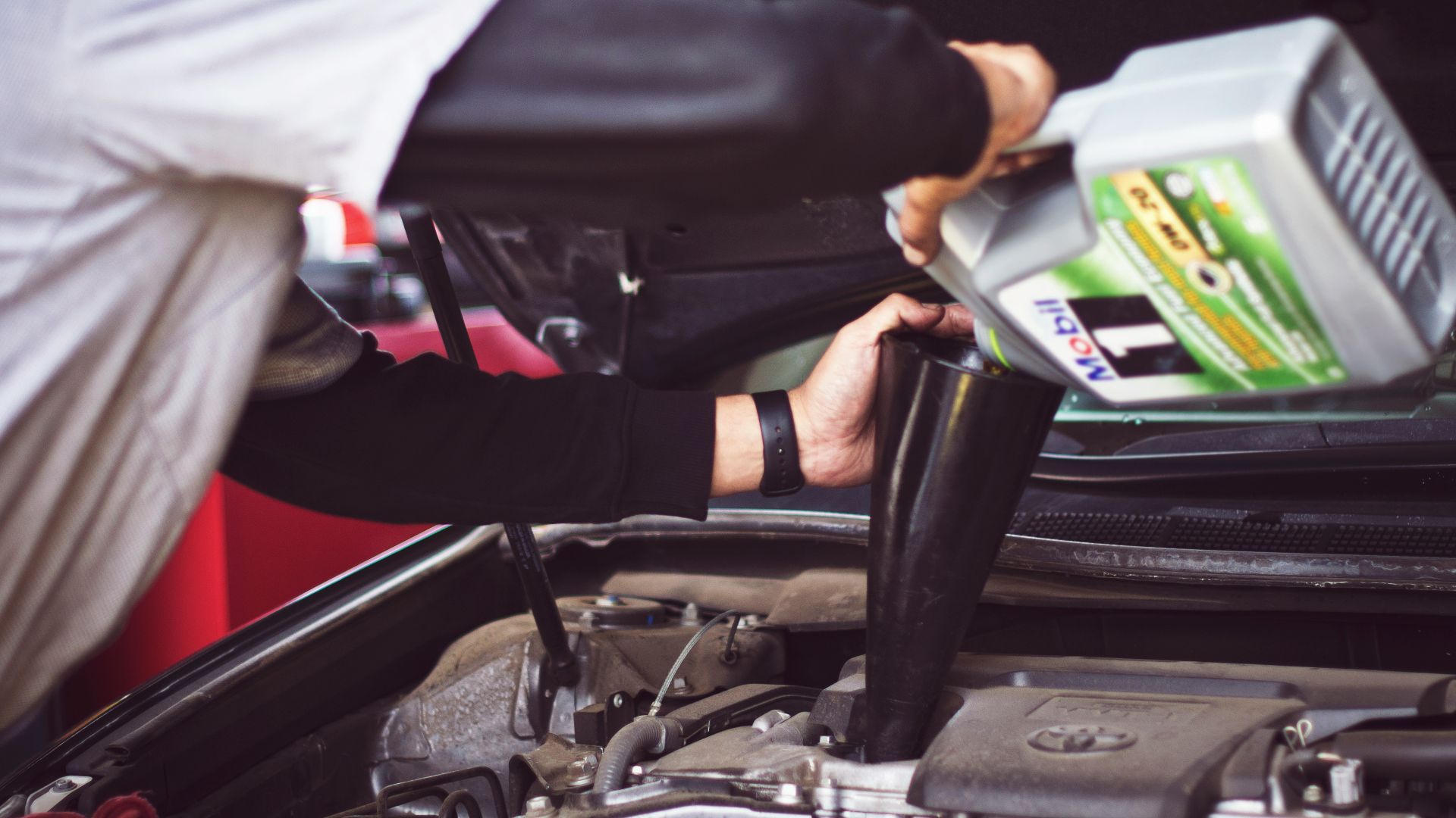 man refilling motor oil on car engine bay
