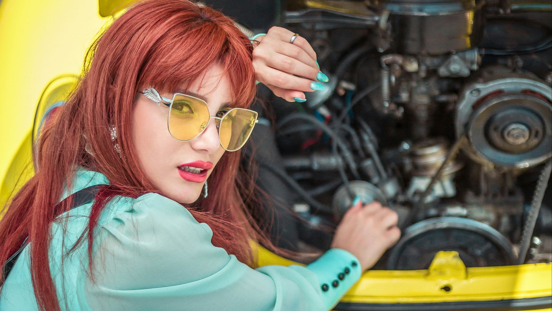 a woman with red hair and sunglasses sitting on the ground next to a yellow car