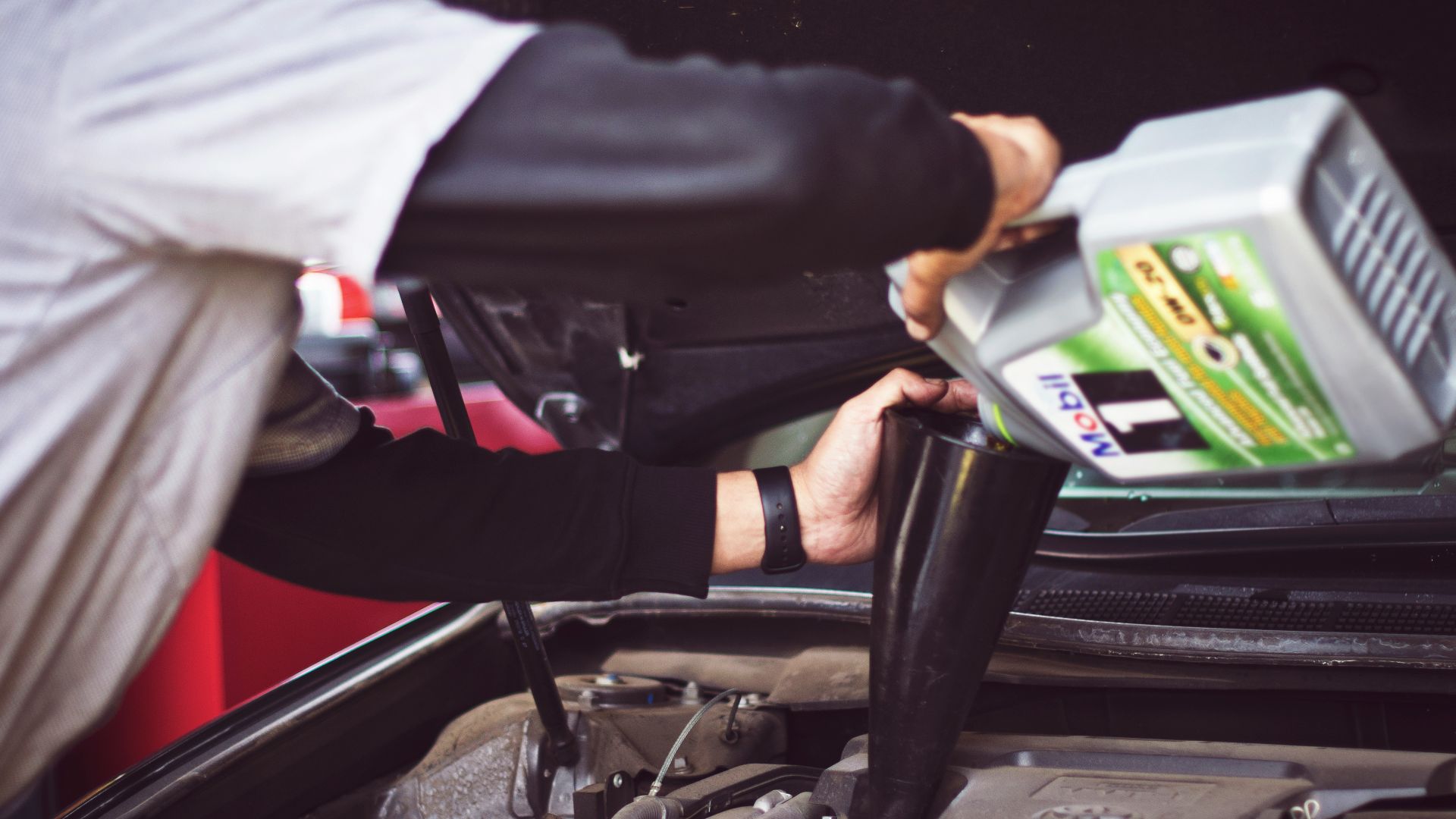 man refilling motor oil on car engine bay