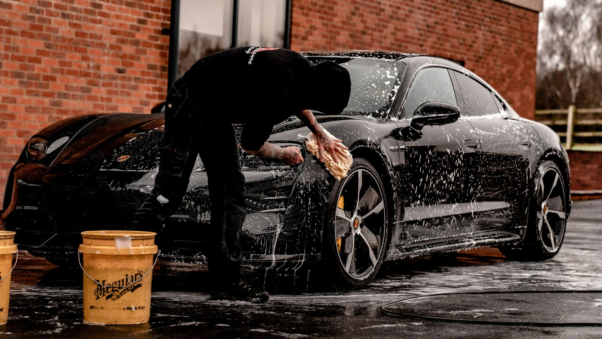 man in black jacket and pants leaning on black car