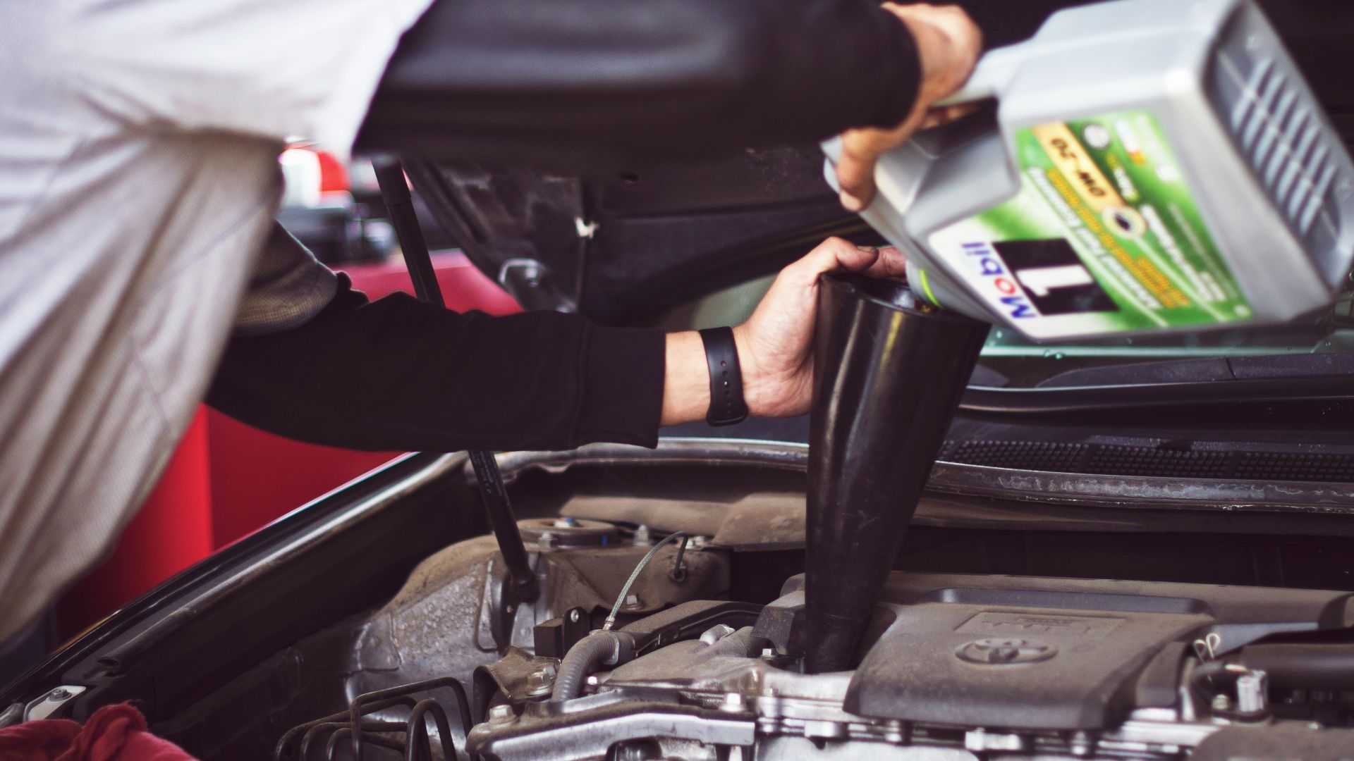 man refilling motor oil on car engine bay