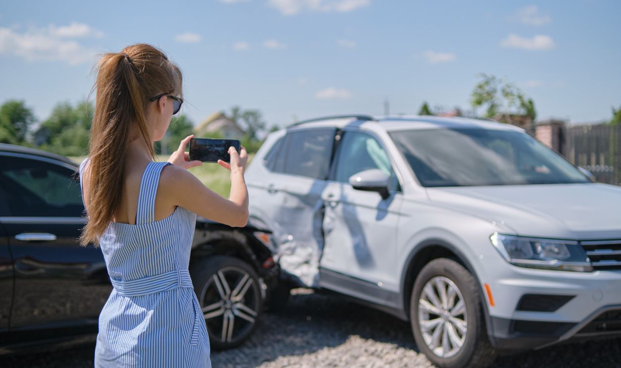 Stressed driver taking picture on sellphone camera of smashed vehicle calling for emergency service help after car accident. Road safety and insurance concept