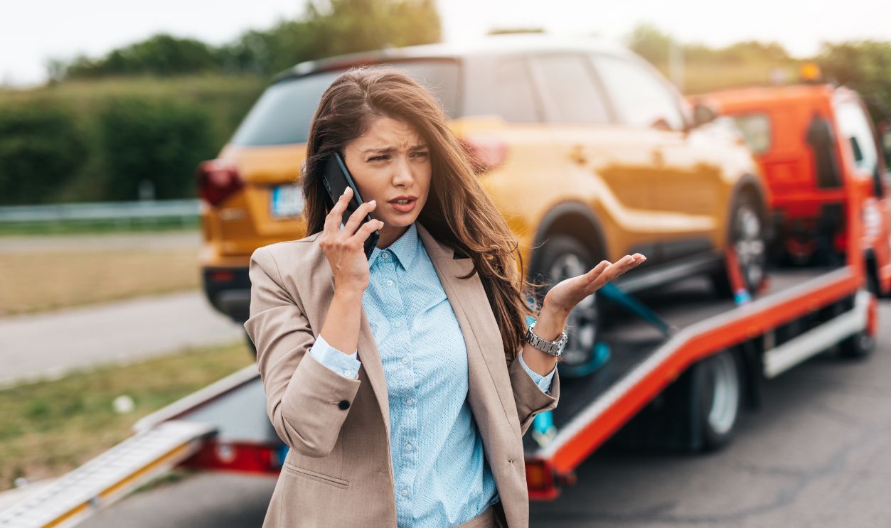 Elegant middle age business woman calling someone while towing service helping her on the road. Roadside assistance concept.