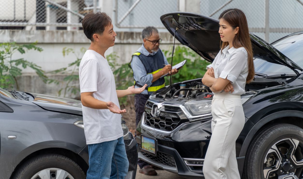 An unset young woman talking angryly to a man who accidentally drove his car and hit her car while insurance agent checking the damage of the accident