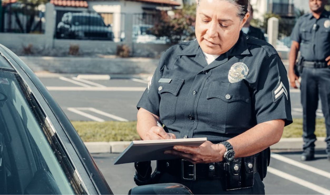A Police Officer Standing Beside a Car while Holding a Clipboard