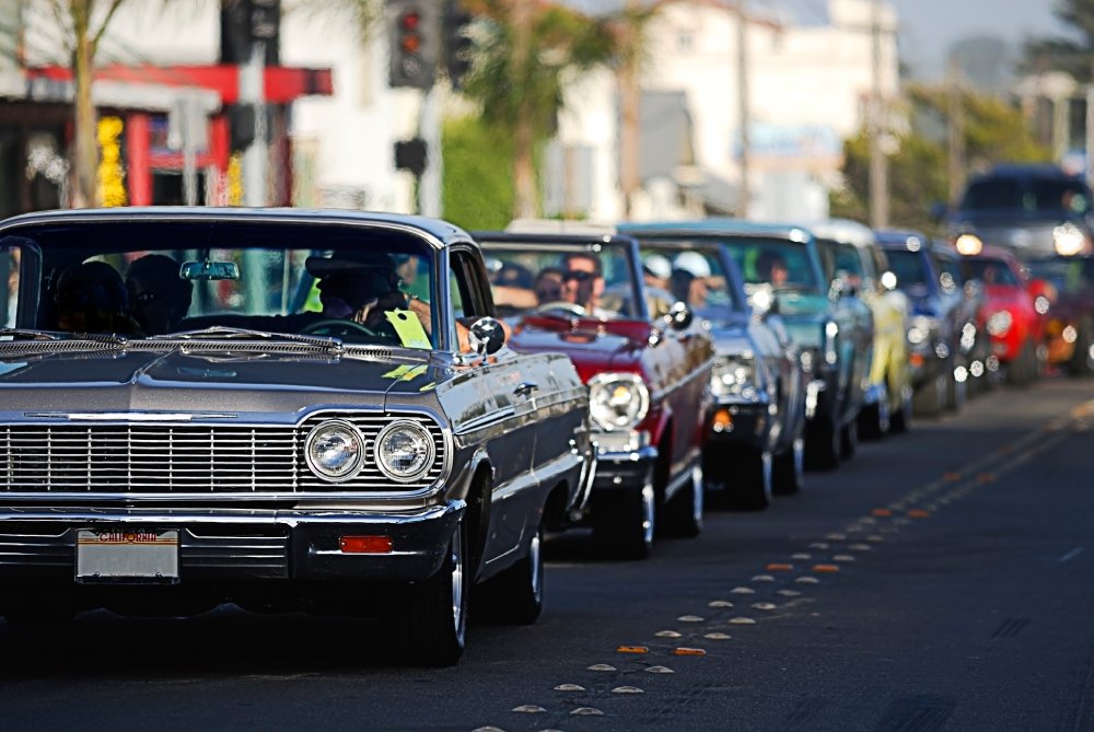 Classic Chevrolet Impala cars driving in a parade or cruise event on a sunny day