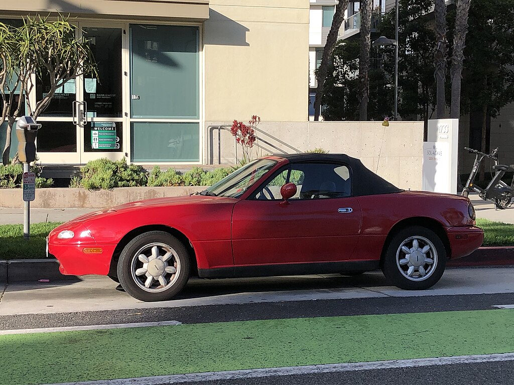 A close-up photo of a 1989 Mazda Miata car parked on a city street