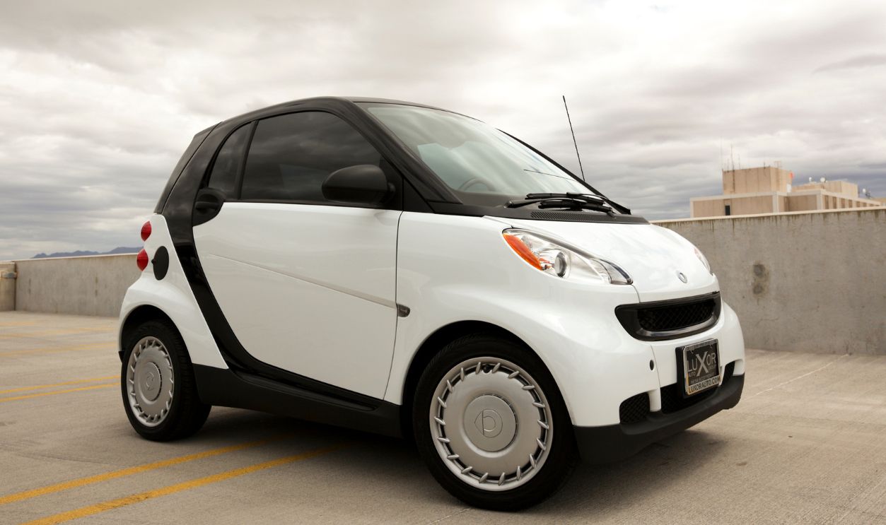 A photo of a parked white Smart Car. The Smart car is a very small and compact car that first debuted in 1998 by Daimler-Benz.