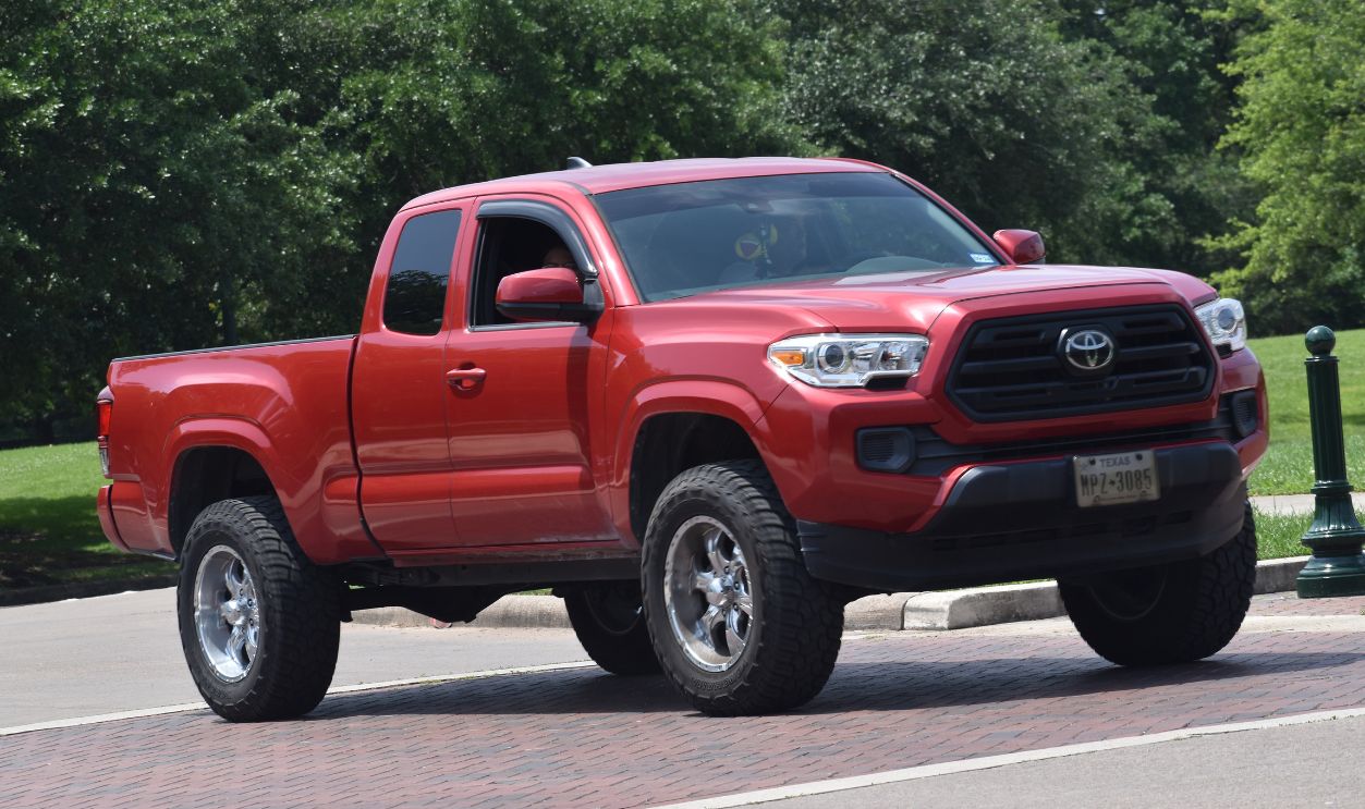 A red Toyota Tacoma cruising near a nature reserve