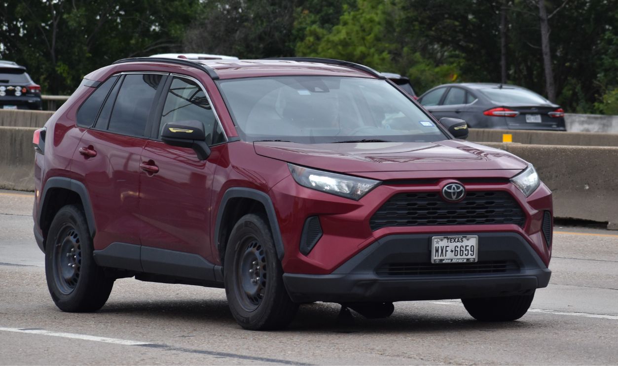A portrait of a maroon Toyota Rav 4 traveling down a highway in moderate traffic