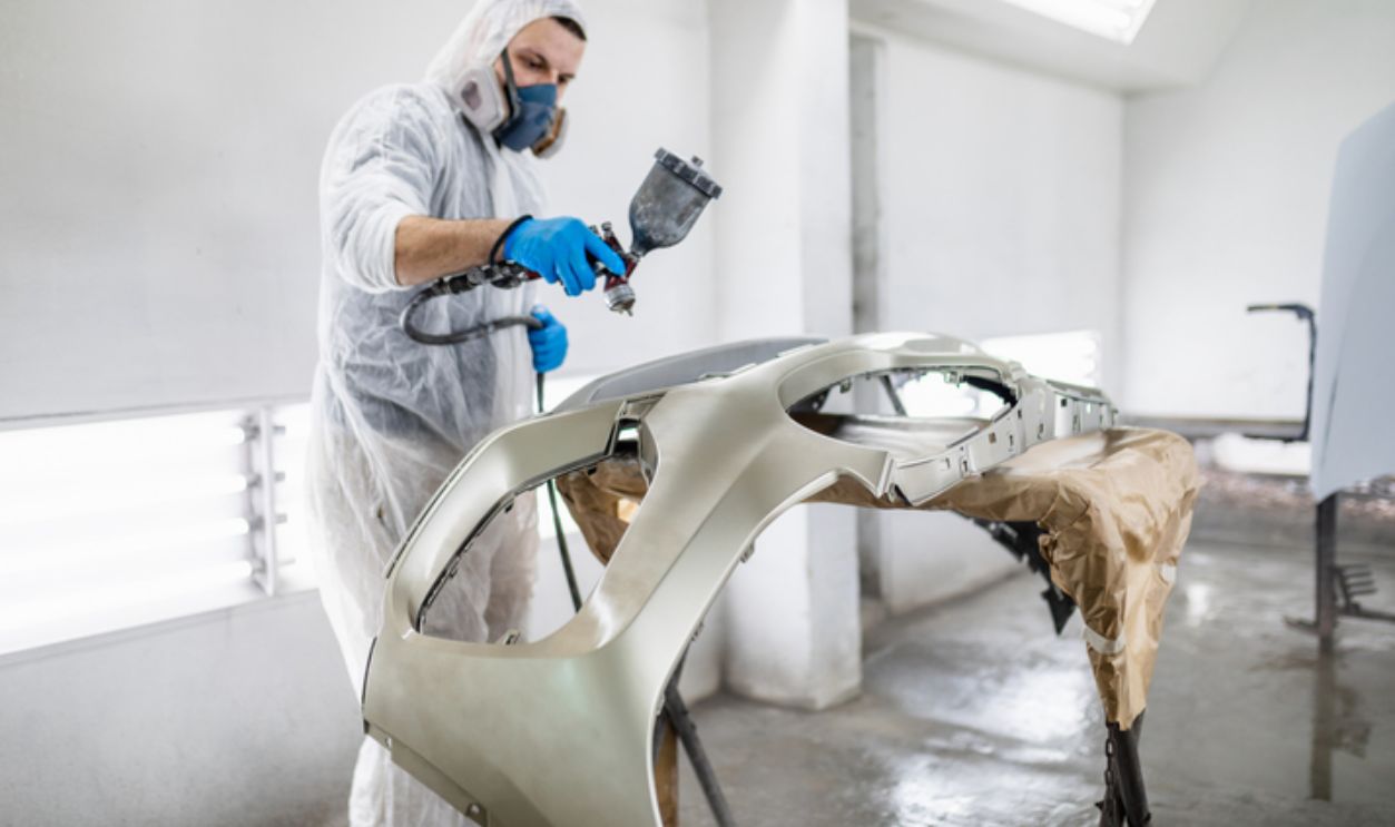 Man with protective clothes and mask painting car using spray compressor.