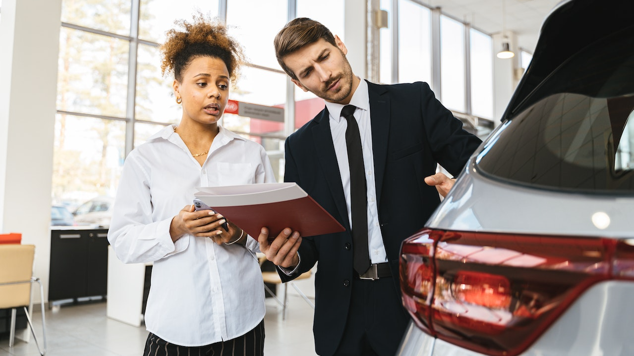 Woman in white shirt talking with a man in car dealership.