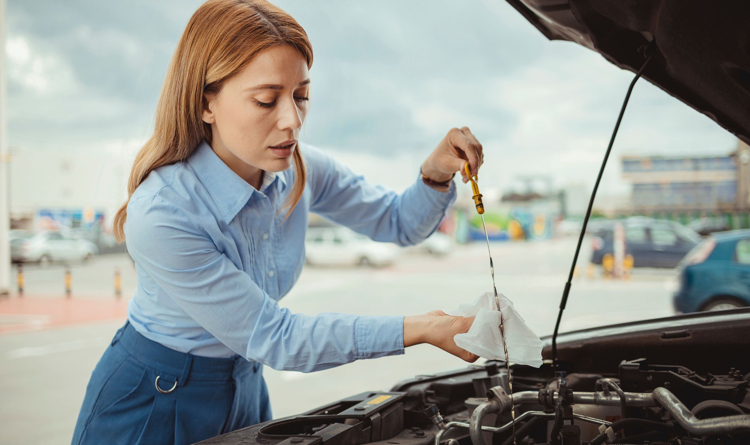 Woman driver checking level of oil on a car engine dipstick