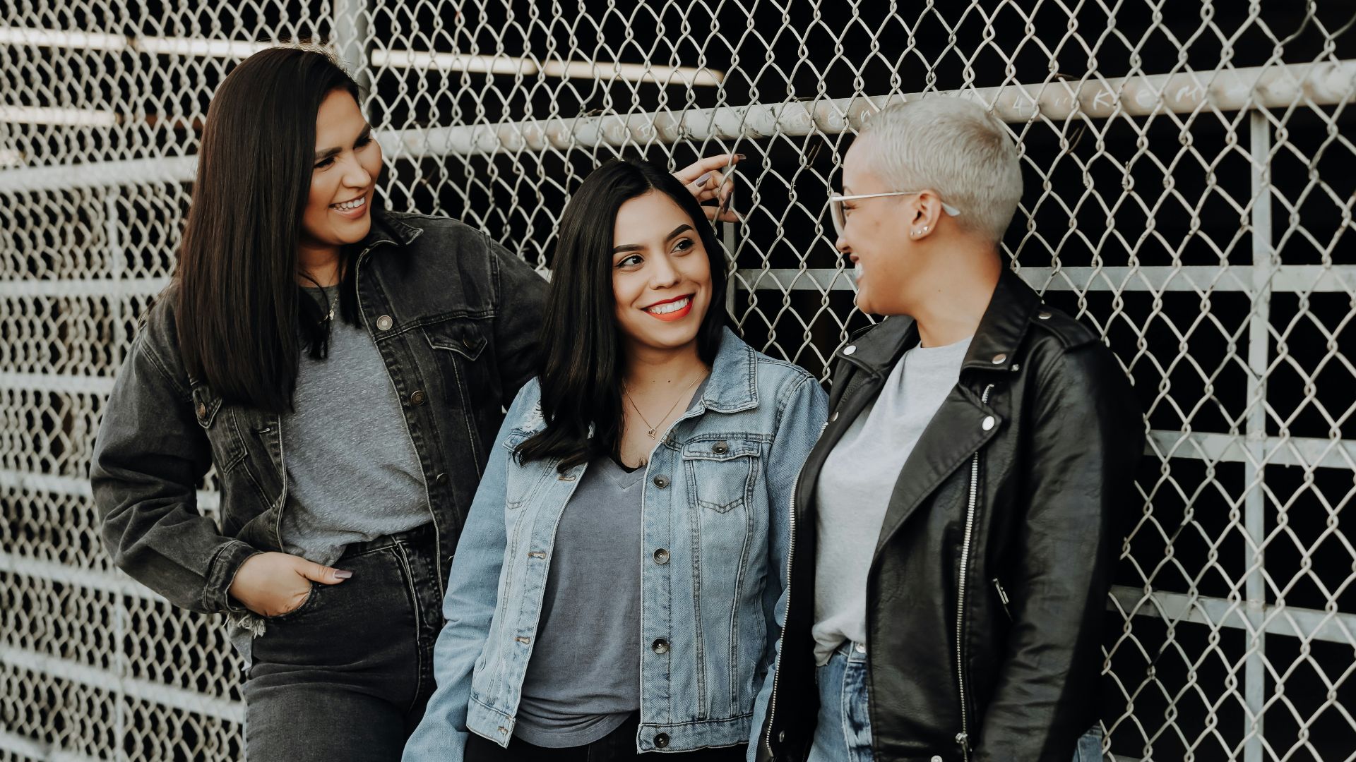 3 women standing beside gray metal fence