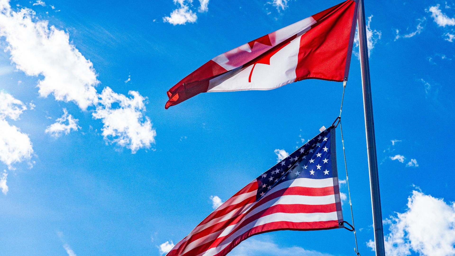 two american and canadian flags flying in the wind