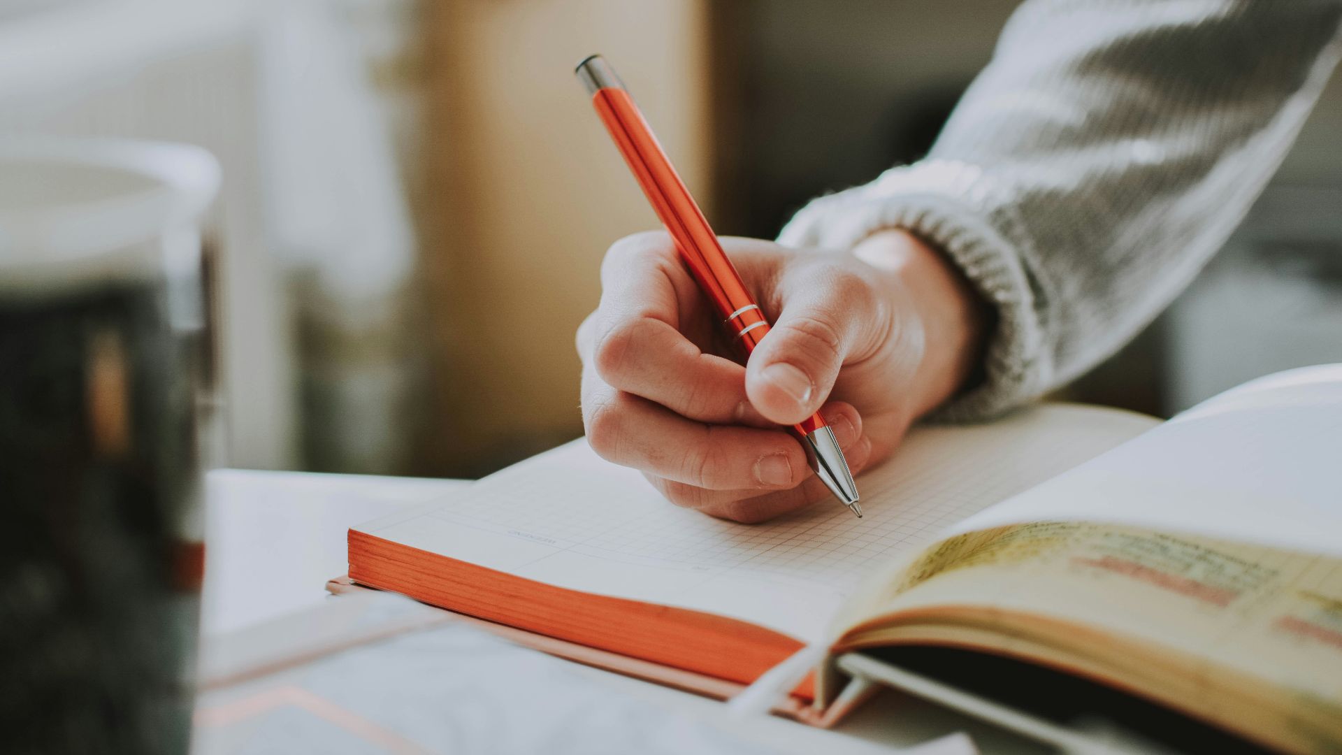 person holding on red pen while writing on book