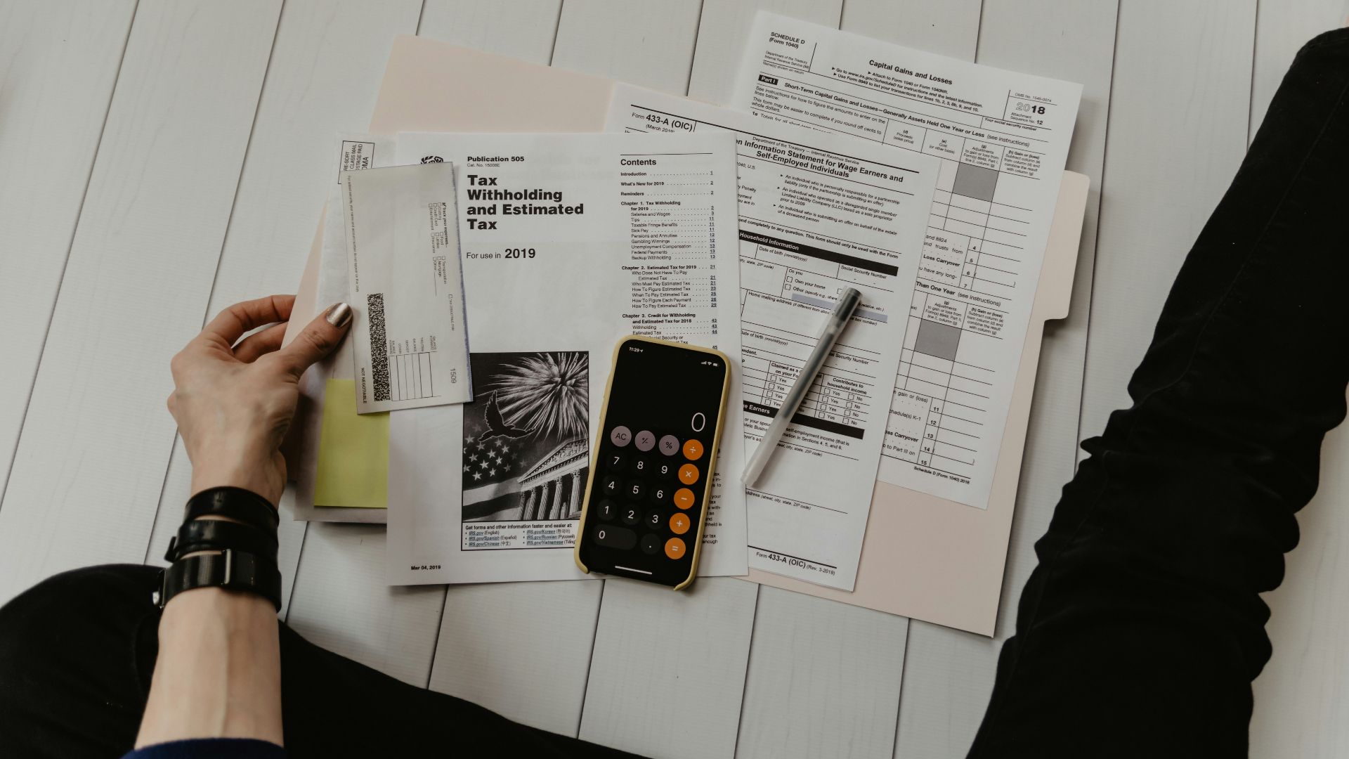 person holding paper near pen and calculator