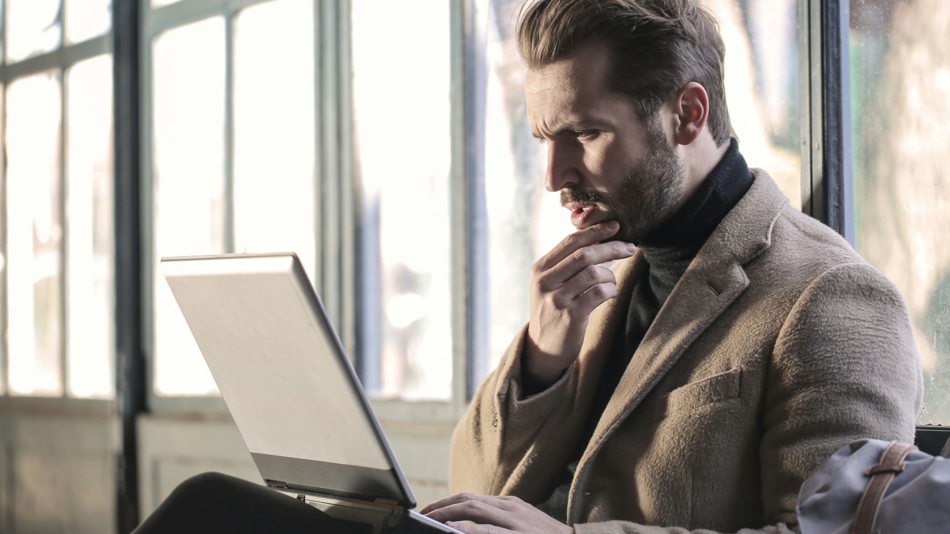 man holding his chin facing laptop computer