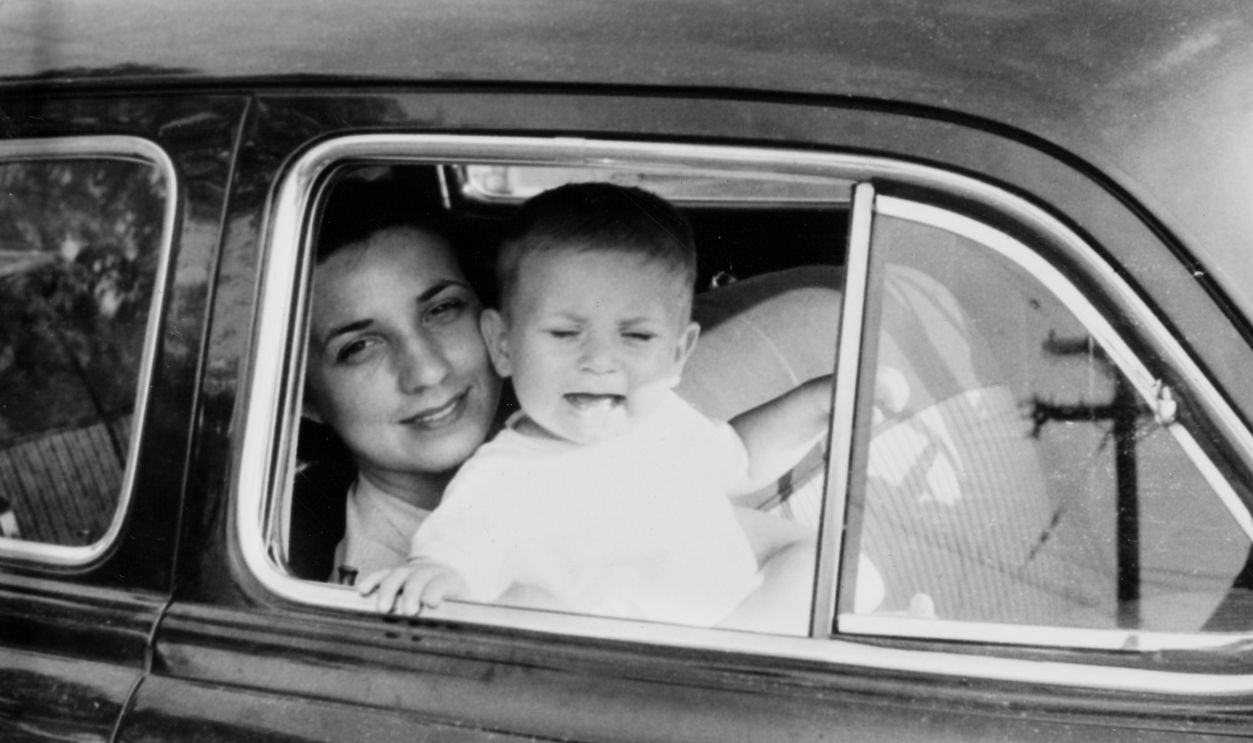 Mother holds crying son in her lap in car, ca. 1954 