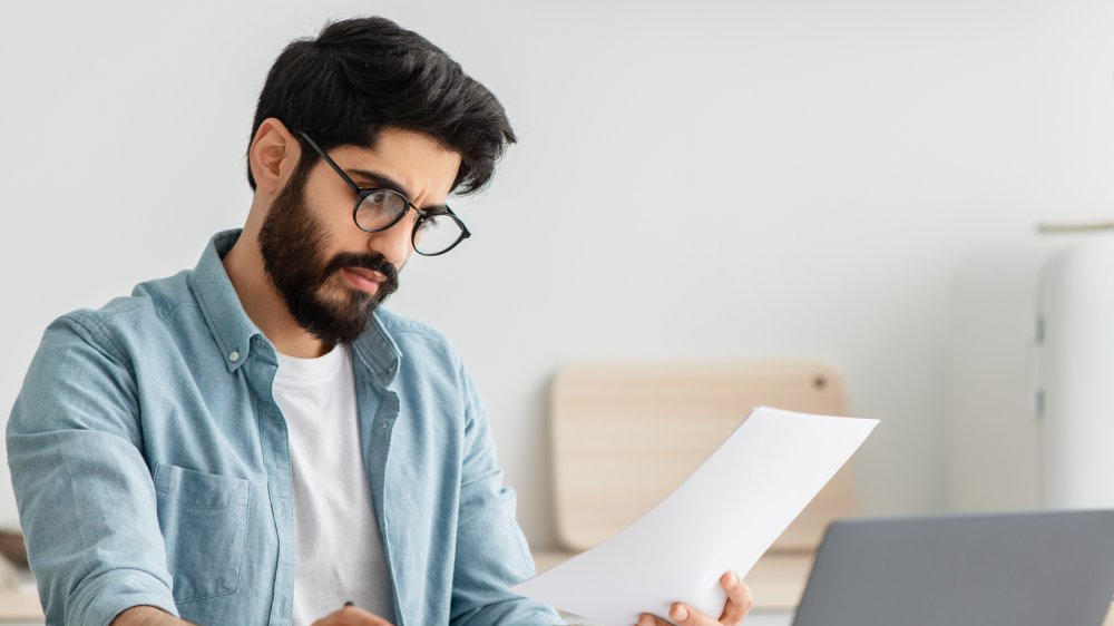 Young man using calculator and laptop computer, sitting at kitchen